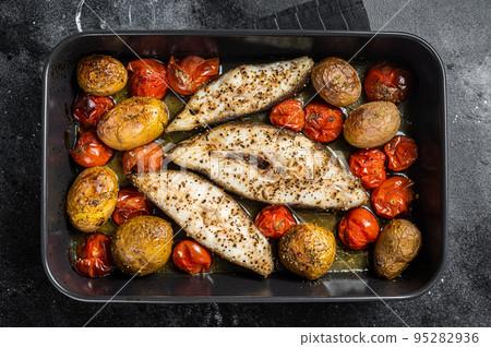 Roasted halibut fish steaks with tomato and potato. Black background. Top view Roasted halibut fish steaks with tomato and potato. Black background. Top view 95282936