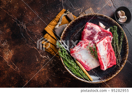 Uncooked Raw veal Short Ribs on rustic plate with rosemary. Dark background. Top view. Copy space Uncooked Raw veal Short Ribs on rustic plate with rosemary. Dark background. Top view. Copy space 95282955