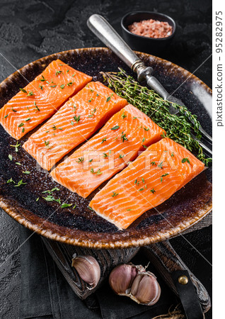 Salmon fillet steaks, raw fish with thyme and herbs. Black background. Top view Salmon fillet steaks, raw fish with thyme and herbs. Black background. Top view 95282975