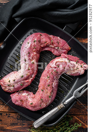 Raw Tenderloin pork fillet ready for cooking, uncooked meat in grill pan with herbs and olive oil. Wooden background. Top view 95282977