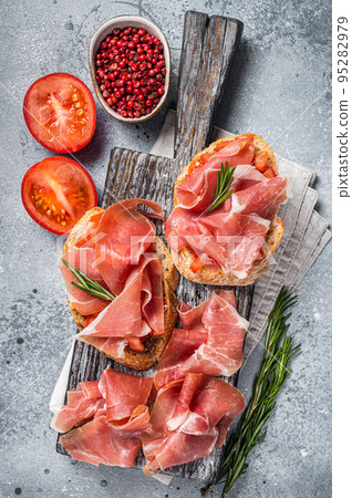 Spanish Tapas - Toast with tomatoes and cured Slices of jamon iberico ham on wooden board. Gray background. Top view Spanish Tapas - Toast with tomatoes and cured Slices of jamon iberico ham on wooden board. Gray background. Top view 95282979