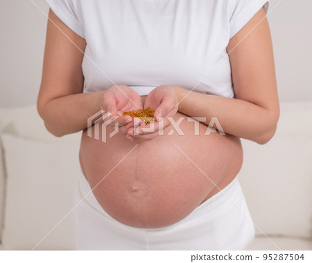 A pregnant woman with a bare belly holds a handful of vitamins. Transparent golden pills. Vitamin D for the expectant mother. 95287504