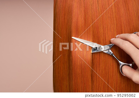Hairdresser cuts long red hair with scissors Hairdresser cuts long red hair with scissors 95295002