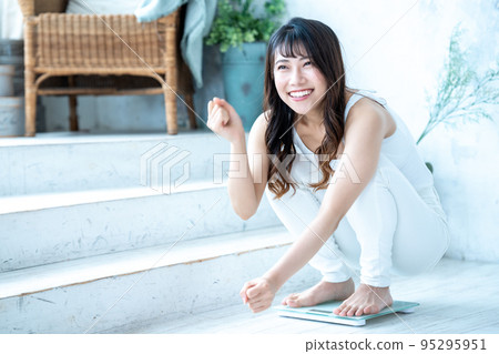 一位年輕女子樂於測量她的體重 95295951