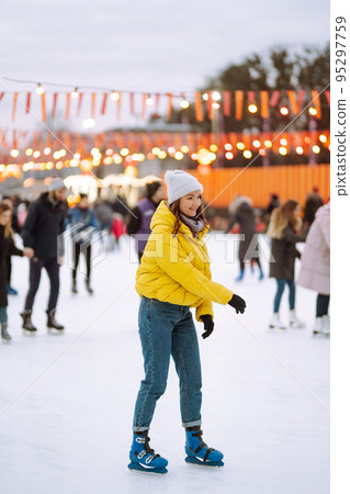 Happy woman ice skating on the ice arena in the city square on Festive Christmas fair. Cold weather. 95297759