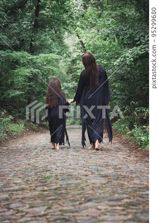 A young witch and her daughter are walking through a forest A young witch and her daughter are walking through a forest 95299680