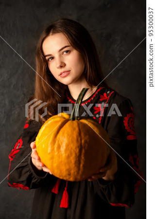 A young girl in a Ukrainian dress holds a pumpkin in her hands 95300037