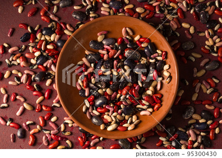 bowl with beans on a burgundy background with scattered beans 95300430