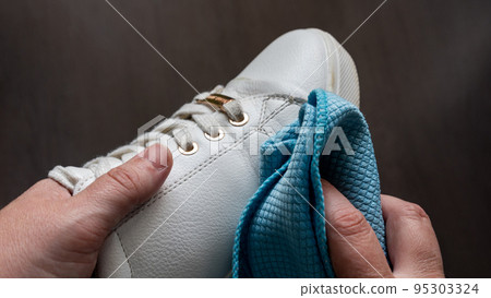 Hands cleaning a white sneaker, with out of focus background 95303324