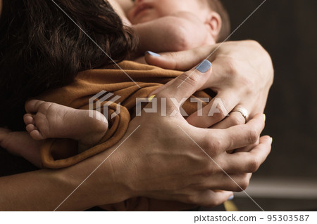 A newborn baby lies in his mother's arms 95303587