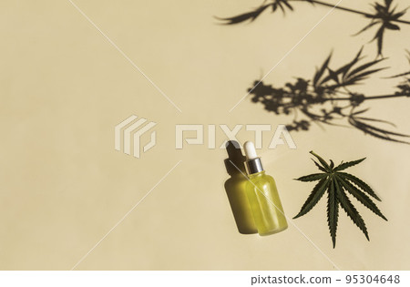 glass bottle with CBD oil, THC tincture on a pastel background with cannabis leaves shadows. minimalism. Cosmetics 95304648