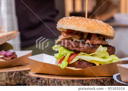Fresh large burger with meat cutlet and bacon on counter for sale - close up Fresh large burger with meat cutlet and bacon on counter for sale - close up 95305016