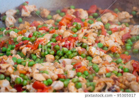 Process of cooking paella with meat pieces, peppers, peas in huge wok - close up 95305017