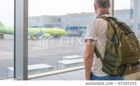 a male traveler with a backpack on his back is waiting for landing on the background of an airplane. Travel concept. Aircraft preparation before takeoff. 95305343