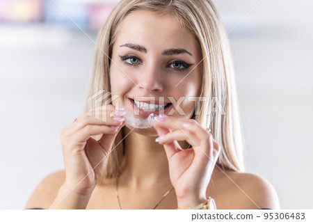 Portrait of beautiful young woman with perfect teeth   holding orthodontic retainers in dental clinic 95306483