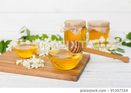 Sweet honey jar surrounded spring acacia blossoms. Honey flows from a spoon in a jar. jars of clear fresh acacia honey on wooden background 95307584