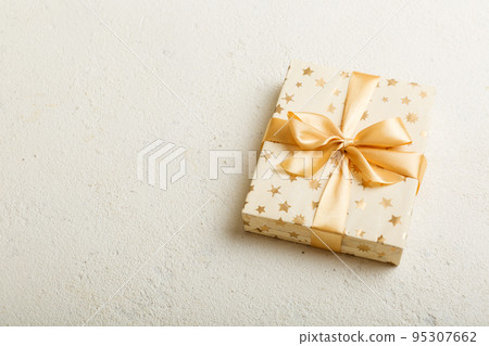 wrapped Christmas or other holiday handmade present in white paper with gold ribbon on colored background. Present box, decoration of gift on colored table, top view with copy space 95307662
