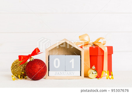 1 january. Christmas composition on colored background with a wooden calendar, with a gift box, toys, bauble copy space 1 january. Christmas composition on colored background with a wooden calendar, with a gift box, toys, bauble copy space 95307676