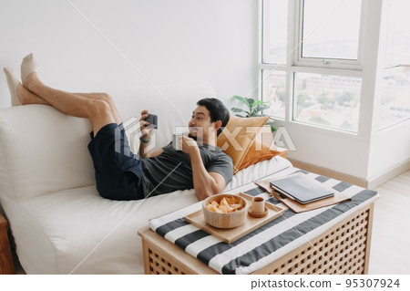 Man watch online tv and eating snack instead of working from home. Man watch online tv and eating snack instead of working from home. 95307924