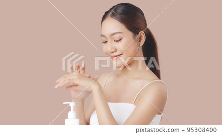 Beautiful young Asian woman applying moisturizing cream lotion on hands isolated on brown background. 95308400