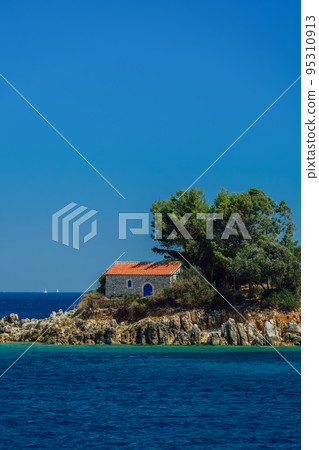 Stone-built Greek Orthodox church with red tiles roof built on a rocky island. Stone-built Greek Orthodox church with red tiles roof built on a rocky island. 95310913
