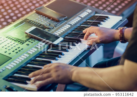 Musician play electronic keyboard synthesizers by using smartphone as guidelines for playing on the concert stage. Selective focus on smartphone. 95311642