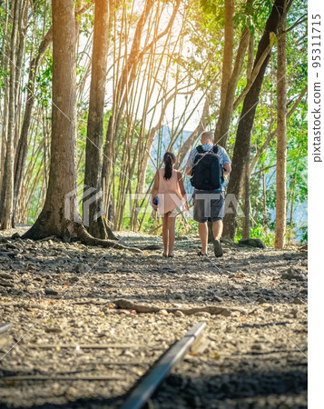 Back view of male tourist and his daughter walking together in forest nature path walk on trail woods background at Hellfire Pass in Kanchanaburi Thailand. Happy people relaxing on active outdoor. Back view of male tourist and his daughter walking together in forest nature path walk on trail woods background at Hellfire Pass in Kanchanaburi Thailand. Happy people relaxing on active outdoor. 95311715