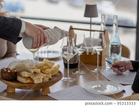Sommelier pouring white wine into glasses with hidden bottle 95313333