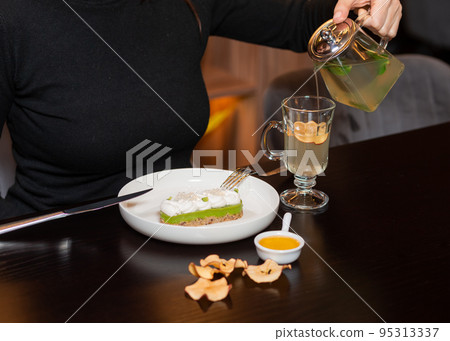 Cropped view of woman in black turtleneck pouring brewed green tea Cropped view of woman in black turtleneck pouring brewed green tea 95313337