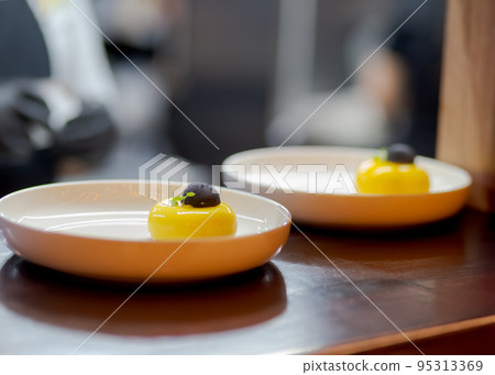 Yellow cheesecake dessert in white plate with black chocolate. 95313369