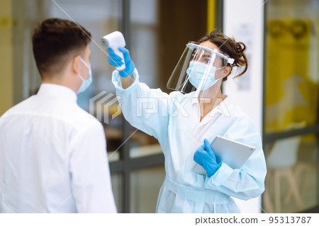 Temperature screening office workers. Disease control expert in visor with an Infrared thermometer. Temperature screening office workers. Disease control expert in visor with an Infrared thermometer. 95313787