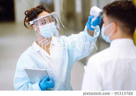 Temperature screening office workers. Disease control expert in visor with an Infrared thermometer. Temperature screening office workers. Disease control expert in visor with an Infrared thermometer. 95313788