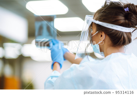 A female doctor in visor and protective gloves examines an X-ray of a patient A female doctor in visor and protective gloves examines an X-ray of a patient 95314116