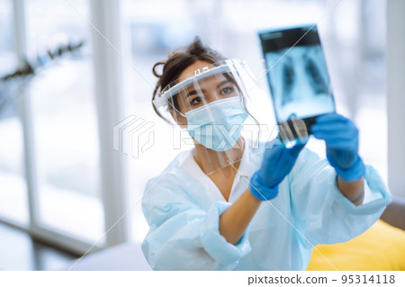 A female doctor in visor and protective gloves examines an X-ray of a patient 95314118