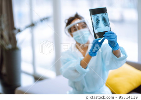 A female doctor in visor and protective gloves examines an X-ray of a patient 95314119