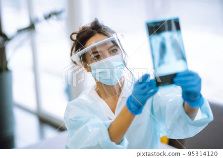 A female doctor in visor and protective gloves examines an X-ray of a patient A female doctor in visor and protective gloves examines an X-ray of a patient 95314120