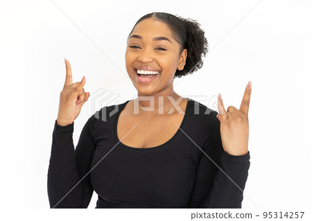 Portrait of laughing young woman making rock and roll gesture 95314257