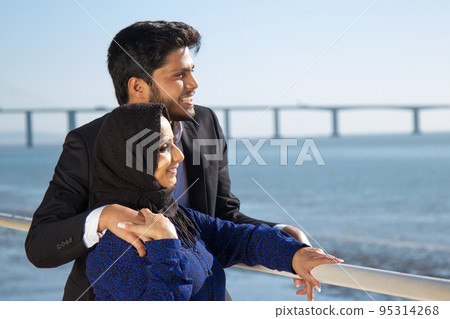 Side view of young couple in love standing near fence Side view of young couple in love standing near fence 95314268