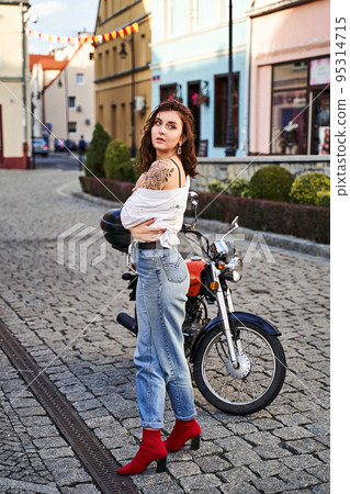 Young beautiful woman in unbottend shirt with a tattoo on her shoulder standing by a bike on the street Young beautiful woman in unbottend shirt with a tattoo on her shoulder standing by a bike on the street 95314715