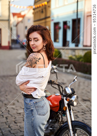 Young beautiful woman shows her bare shoulder with a tattoo standing by a bike on the street Young beautiful woman shows her bare shoulder with a tattoo standing by a bike on the street 95314716
