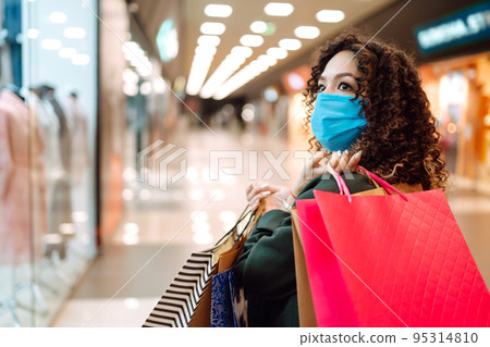 Young woman wearing protection face mask against coronavirus after shopping in the mall. Covid-2019. 95314810
