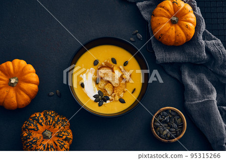 Pumpkin cream soup with seeds on dark background Pumpkin cream soup with seeds on dark background 95315266