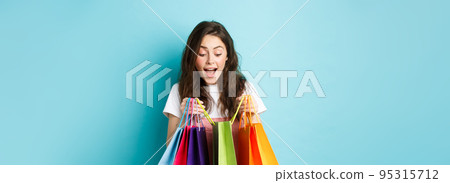 Image of happy young woman carry lots of shopping bags, buying things on spring discounts, standing over blue background Image of happy young woman carry lots of shopping bags, buying things on spring discounts, standing over blue background 95315712