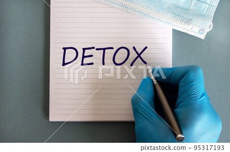 Male doctors hand in blue glove writes the word 'detox' on a white note. Medicine mask. Beautiful blue background. Male doctors hand in blue glove writes the word 'detox' on a white note. Medicine mask. Beautiful blue background. 95317193