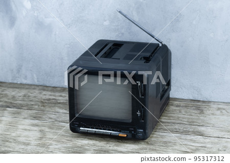 Vintage retro analog small TV set stand on wooden floor front grey concrete wall background. 95317312