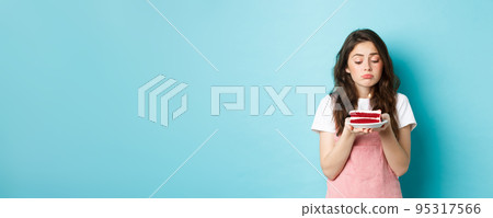 Holidays and celebration. Sad cute girl celebrating her birthday alone, holding cake on plate with one candle and sulking upset, standing lonely against blue background 95317566