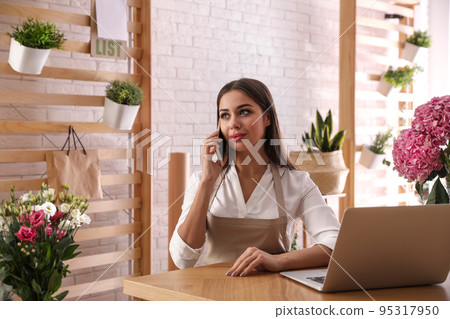Florist talking on smartphone near laptop in workshop 95317950