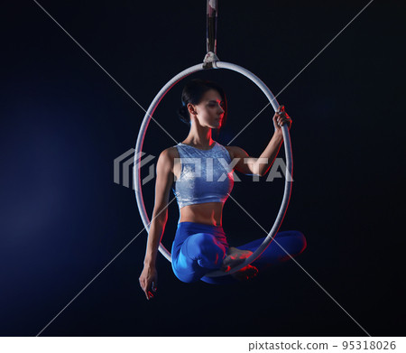 Young woman performing acrobatic element on aerial ring against dark background. Space for text Young woman performing acrobatic element on aerial ring against dark background. Space for text 95318026