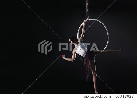 Young woman performing acrobatic element on aerial ring against dark background. Space for text 95318028