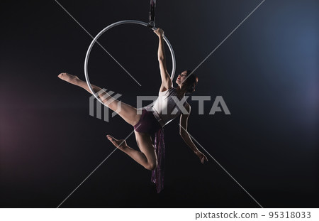 Young woman performing acrobatic element on aerial ring indoors 95318033